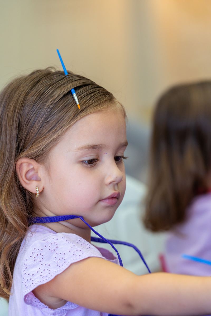 Niña concentrada en clase de pintura con un pincel en el cabello